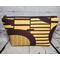 Front of a golden yellow and brown abstract African print large makeup bag featuring a gunmetal zipper and metal Bass Creations logo.