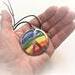 2 inch diameter copper enamel rainbow with peace symbol in a hand to show size relationship