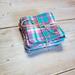 side view of a pink and teal plaid reusable facial square.