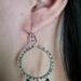 Person models one emerald green and silver wire wrapped dangle earring.