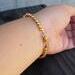 The underside of the bracelet. Two sizes of round gold beads clasped around the wrist and the extender hanging. 