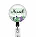 Green and purple flowers with the  name Hannah in black on a light green background affixed to a black retractable badge reel.