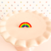 Pair of half-rainbow earrings arranged to make a full arch on a miniature, soft pink cupcake stand in front of a pastel polka-dot background