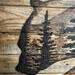 This picture shows a close-up of the bear's head. There are fir trees drawn inside it. It shows the distressed texture of the wood pallet. 