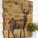 Wood wall art featuring a deer with antlers. The inside of the deer has a pine forest drawing.  The deer is wood-burned onto an old fence. 