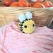 Yellow Bumblebee plushie resting on pink yarn in front of a fruit basket with mandarin oranges.