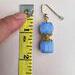 One blue earring lays on a table beside a measuring tape.  The earring measures 1.75 inches long.