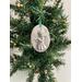 Hancrafted oval holiday ornament with a flutist angel. Ornament is made of plaster of paris, sanded, seal coated, and painted with silver glitter paint. Measurements: Oval 3.5" tall by 2.5" width at the middle,