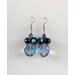 This pair of dangle earrings features a large blue faceted glass bead that switches to purple in the light. There are 4 black round beads seated on top of that with an AB finish on them, bringing out purples, blues, greens, and yellows. Then another purple bead on top with an AB finish and they are connected to a silver earring hook.