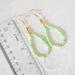 Green gemstone dangle earrings, with gold crystal accents, shown next to a ruler.