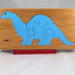 This is a handmade wooden dinosaur tray puzzle with a baby blue dinosaur. The tray is finished with amber shellac. It is lightly used but in like-new condition. This dinosaur is a freestanding and versatile toy for kids of all ages.