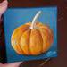 Small square painting of little orange pumpkin with teal blue background.