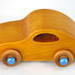 Handmade wooden toy car with an amber shellac finish and metallic sapphire blue trim, modeled after the classic 1957 Bug.