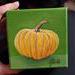 Photo of small square canvas painting of orange pumpkin with a olive green background