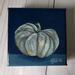 Photo of small square canvas painting of oddly shaped light blue pumpkin with a dark blue background