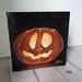 Photo of small square canvas painting of glowing jack o'lantern pumpkin with a black background