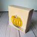Photo of small square canvas painting of orange pumpkin with peach colored background