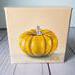 Photo of small square canvas painting of orange pumpkin with peach colored background