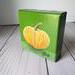 Photo of small square canvas painting of orange pumpkin with a olive green background
