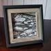 Photo of small drawing of rocks in black and white ink, framed with a black and grey frame