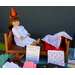 A cherry doll bed for 18" dolls has an American Girl doll in a white nightgown with pink spots sitting on it.  She wears an orange witch's hat in season for Halloween and has a doll quilt at her feet.