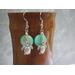 Sea turtle charm earrings set against a green shell disc bead in a soft green, the little turtle dangles freely on a short length of chain. 