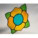 A bright stained glass yellow flower with teal center and green leaves, on a neutral background