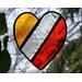 Stained glass heart with red, clear, and orange stripes with nature in the background