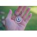 Lifestyle image of hand holding keepsake key ring with green grassy background.