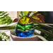 Stained glass Easter Egg tucked into a potted plant with additional plants in the background, Egg features yellow, green, and blue stripes