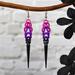 Chainmaille earrings in pink, violet and black. Earrings taper outward slightly before narrowing, and a long black spike hangs at the bottom