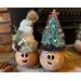 Two Christmas gourds elves are decorating a fireplace hearth. Each elf has a custom hat and a happy face carved out of their gourd shell. 
