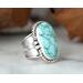Large turquoise blue ovalish stone with embellished setting on a thick wide tapered band with a light patina. Size 9.5
