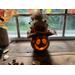 A carved pumpkin gourd decoration. Its happy face is lit with a battery-operated candle. It has pretty fall leaves displayed around it. 