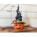 A Halloween pumpkin witch. The witch has a handmade pointy hat decorated with botanicals and fall leaves. It is 13 by 5 inches inches wide. 