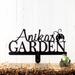 Metal garden sign with first name and ladybug image, in matte black powder coat Placed against a white wood wall.