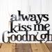 Always Kiss me Goodnight metal wall decor, in raw steel. Placed against a wood wall.