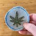 3" round light blue denim patch with a green embroidered hemp leaf in the center.