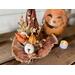 This shows a fall arrangement on the brim of Beatrice's  witch hat. There are orange paper lanterns, a white pumpkin and pine cones. 
