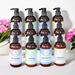 Twelve bottles of luxurious lotions by Whole Self Aromatherapy atop a soft white table linen with pink flowers on either side.