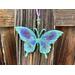 resin butterfly sun catcher hanging on wood fence outdoors in shaded sunlight.