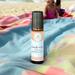 A close-up of a bottle of Beach Vibes wellness blend on a colorful blanket at the beach, with children playing in the blurred background.