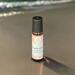 A bottle of Whole Self Aromatherapy's Beach Vibes wellness roller on a wet, sandy beach at sunset, with blurred ocean waves in background.