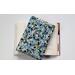A padded book sleeve on top of an open book. The book sleeve is made with a blue floral Rifle Paper Co. cotton print.