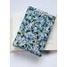 A padded book sleeve on top of an open book. The book sleeve is made with a blue floral Rifle Paper Co. cotton print.