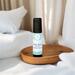 Best Man essential oil roller on a small round wooden dish, surrounded by a stack of white towels and an off-white linen backdrop.