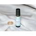 Best Man essential oil roller on fluffy white linen with a shiny gold wedding band sitting along of it.
