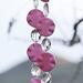 Pink magnesite stone beads shaped as wavy flat rounds are strung with glass crystal ovals and anchored by two pieces of pink fused glass. Hanging from tree.