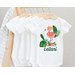 white baby bodysuit with tropical leaves and flowers surrounding a pink flamingo. Baby name at bottom of design in green script to match