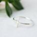 Sleek sterling silver sideways cross ring on white background.
